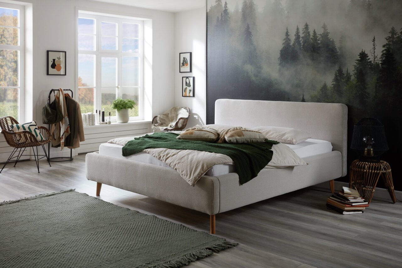 Modernes Polsterbett in einem stilvoll eingerichteten Schlafzimmer mit Waldbild an der Wand, aus der Seitenperspektive fotografiert.