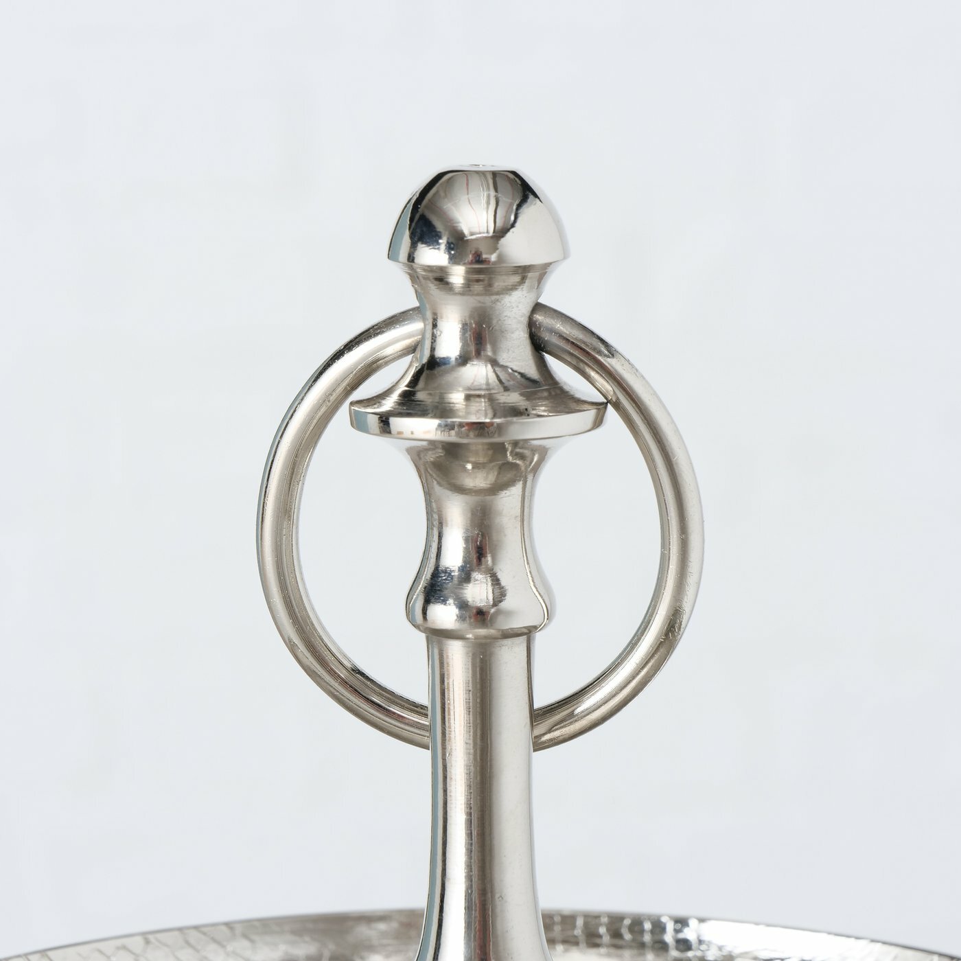 Nahaufnahme des oberen Teils einer silbernen Etagere mit einem dekorativen Griff und einem Ring, aus Aluminium gefertigt.