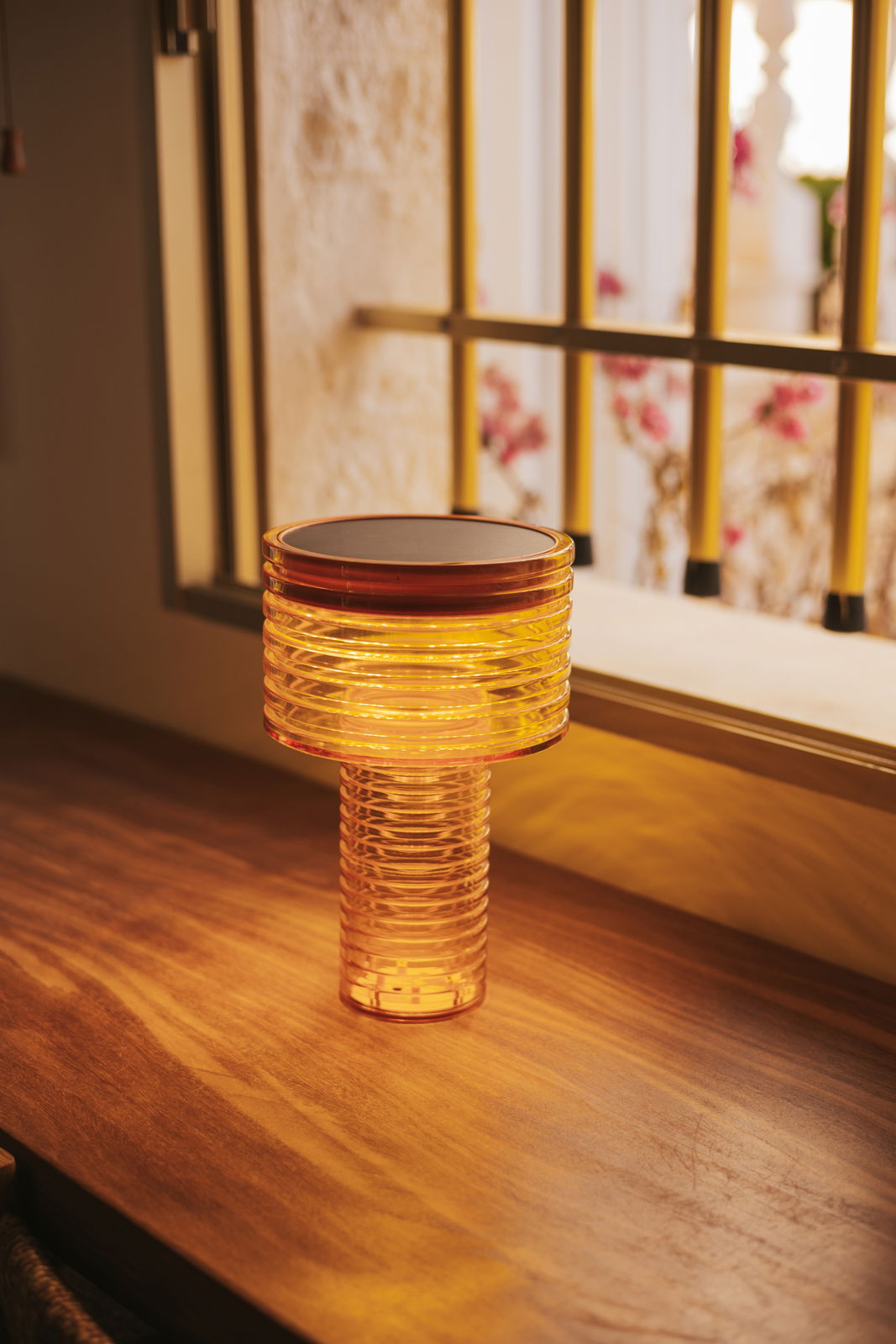 Akku-Solar-Tischleuchte in warmem Licht auf einem Holztisch, seitliche Perspektive.