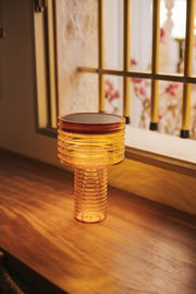 Akku-Solar-Tischleuchte in warmem Licht auf einem Holztisch, seitliche Perspektive.