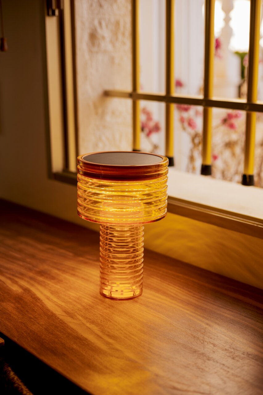 Accu- en zonne-energie-tafellamp met warm licht op een houten tafel, gezien vanaf de zijkant.