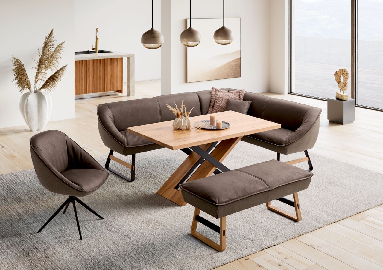 Koinor Armlehnstuhl Moderne Esszimmergarnitur mit Eckbank, Armlehnstuhl und Esstisch aus Holz in einem hellen Raum mit Blick auf die Terrasse, Perspektive von schräg oben.