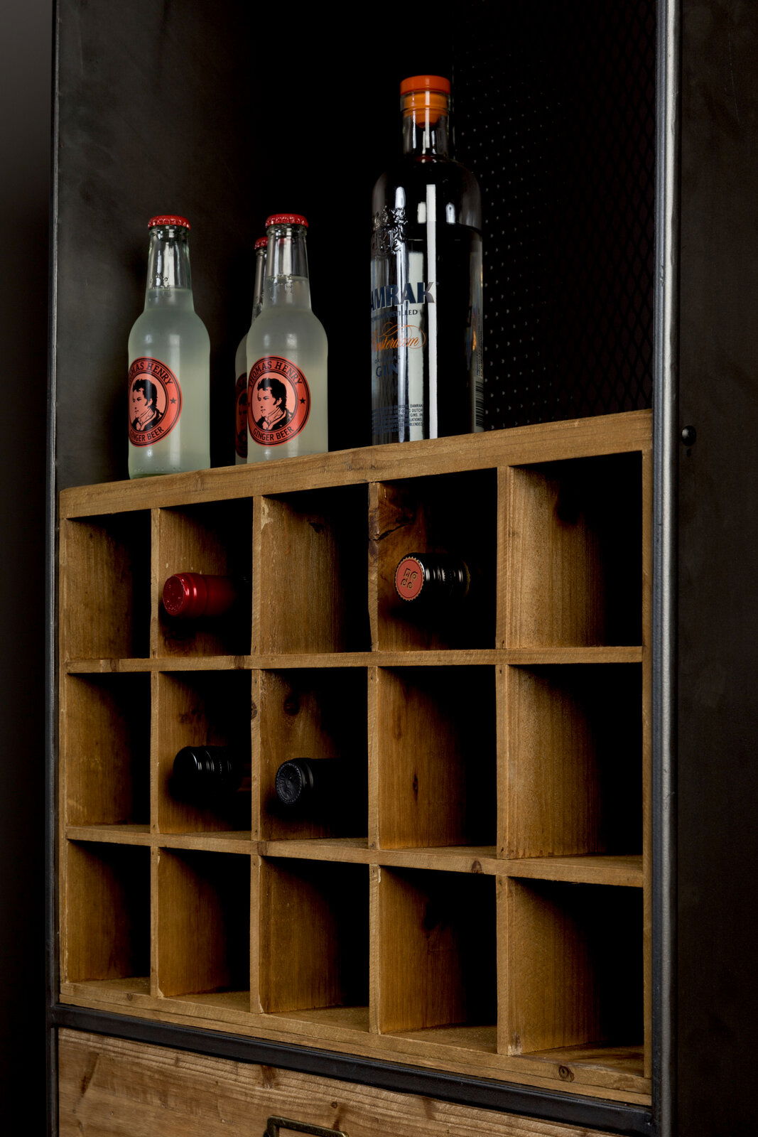 Nahaufnahme eines Weinregals aus Holz mit mehreren Fächern, in denen Weinflaschen horizontal gelagert sind. Oben stehen zwei Flaschen Ginger Beer und eine Flasche Gin. Perspektive von schräg vorne.