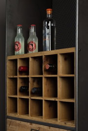 Nahaufnahme eines Weinregals aus Holz mit mehreren Fächern, in denen Weinflaschen horizontal gelagert sind. Oben stehen zwei Flaschen Ginger Beer und eine Flasche Gin. Perspektive von schräg vorne.