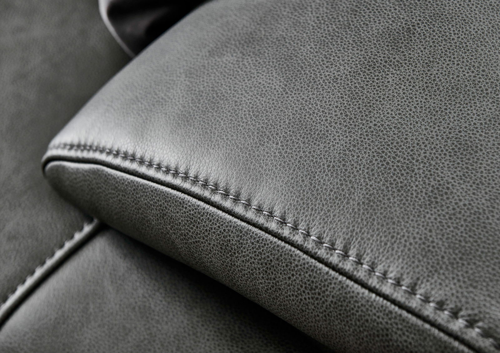 Nahaufnahme einer grauen Ledercouch mit feiner Naht, Perspektive von oben.