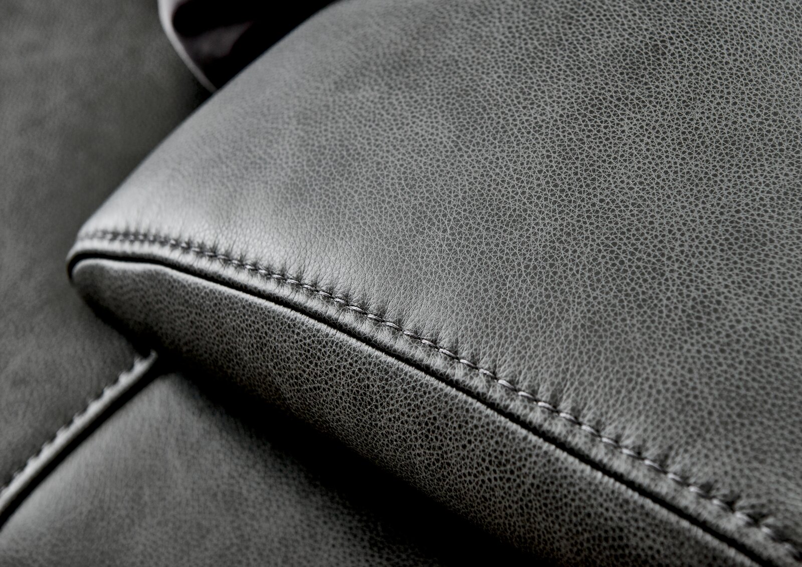 Nahaufnahme einer grauen Ledercouch mit feiner Naht, Perspektive von oben.