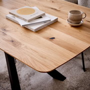 Nahaufnahme eines Esstisches aus Holz mit natürlicher Maserung, darauf liegen Bücher und eine Tasse, Perspektive von schräg oben.