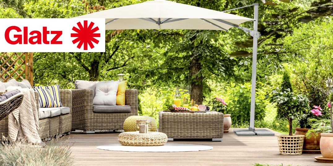 Sitzbereich im Freien mit Korbmöbeln, einem Sonnenschirm im Grünen, mit dem Glatz-Logo.