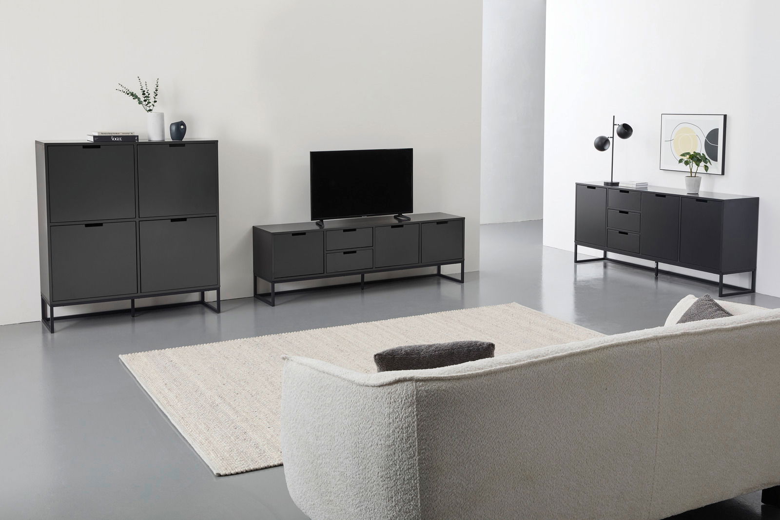 Novel Tv-kast KUNO Moderne Wohnzimmermöbel in schwarzem Design, bestehend aus einem Highboard, einem TV-Lowboard und einem Sideboard, aus der Perspektive eines gemütlichen Wohnzimmers mit Sofa und Teppich.