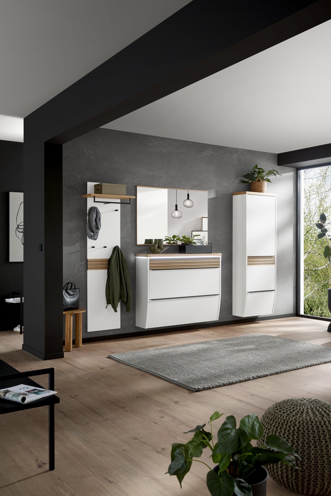 Modernes Flur-Set mit weißen Hängeschränken, Spiegel, Garderobenpaneel und Holz-Akzenten vor grauer Wand, fotografiert in leichter Schrägansicht von vorn.