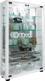 Weiße Glasvitrine mit mehreren Glasböden und Glastüren, gefüllt mit Dekoartikeln, Kamera und CD-Stapeln, fotografiert in schräger Frontansicht von leicht links
