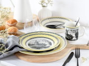Gedeckter Frühstückstisch mit gelb-grau gemustertem Geschirrset (Teller, Schüssel und Tasse mit Windmühlenmotiv), Glas und Besteck auf Holzbrett, fotografiert in leicht erhöhter Frontansicht.