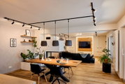 Moderne Wohnküche mit hängenden schwarzen Lampenschirmen über einem Holztisch, seitliche Perspektive.