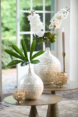 Elegantes Teelicht in goldener, durchbrochener Kugelform auf einem Tisch, umgeben von dekorativen Vasen und Kerzen, aus der Seitenperspektive fotografiert.