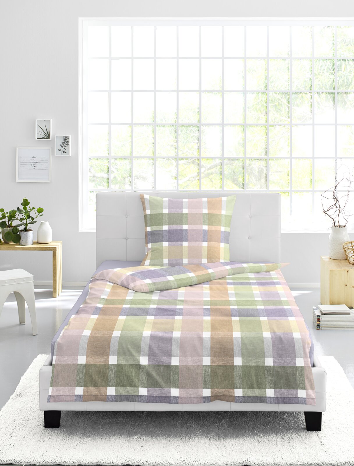 Vooraanzicht van een eenpersoonsbed met geruite beddengoedset in zachte pastelkleuren zoals groen, roze, paars en beige, gestyled in een lichte moderne slaapkamer.