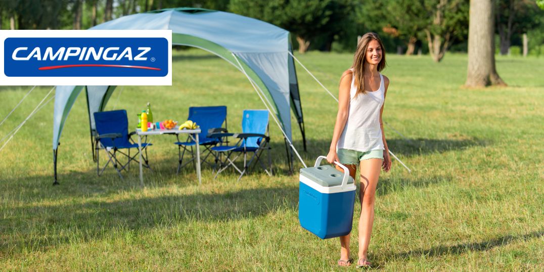 Eine Frau mit einer Kühlbox auf einer Rasenfläche, im Hintergrund sieht man eine Campingstühle und einem Tisch. Oben das Lobo Campingaz
