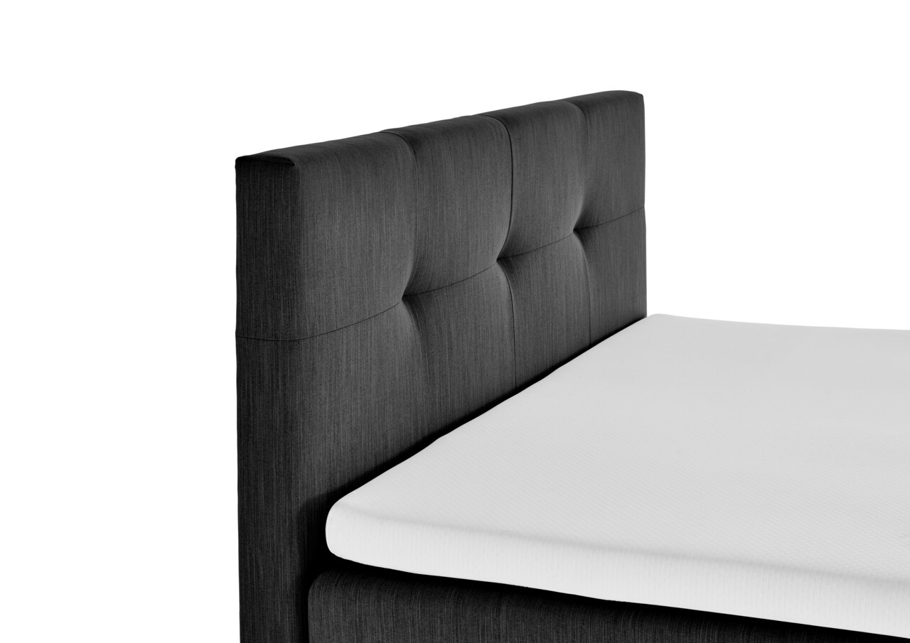 Seitliche Ansicht eines Boxspringbetts mit dunkelgrauem, gestepptem Kopfteil und weißer Matratze.