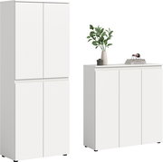 Zwei weiße, grifflose Schränke im minimalistischen Design: links ein hoher Mehrzweckschrank mit vier Türen, rechts ein breites Sideboard mit drei Türen und Deko auf der Ablage; Ansicht schräg von vorn.