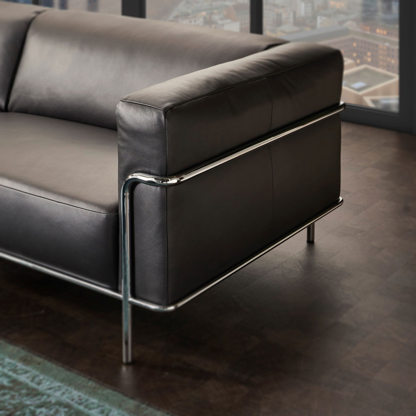 Modernes 3er-Sofa mit schwarzem Lederbezug und verchromtem Metallrahmen, seitliche Perspektive.