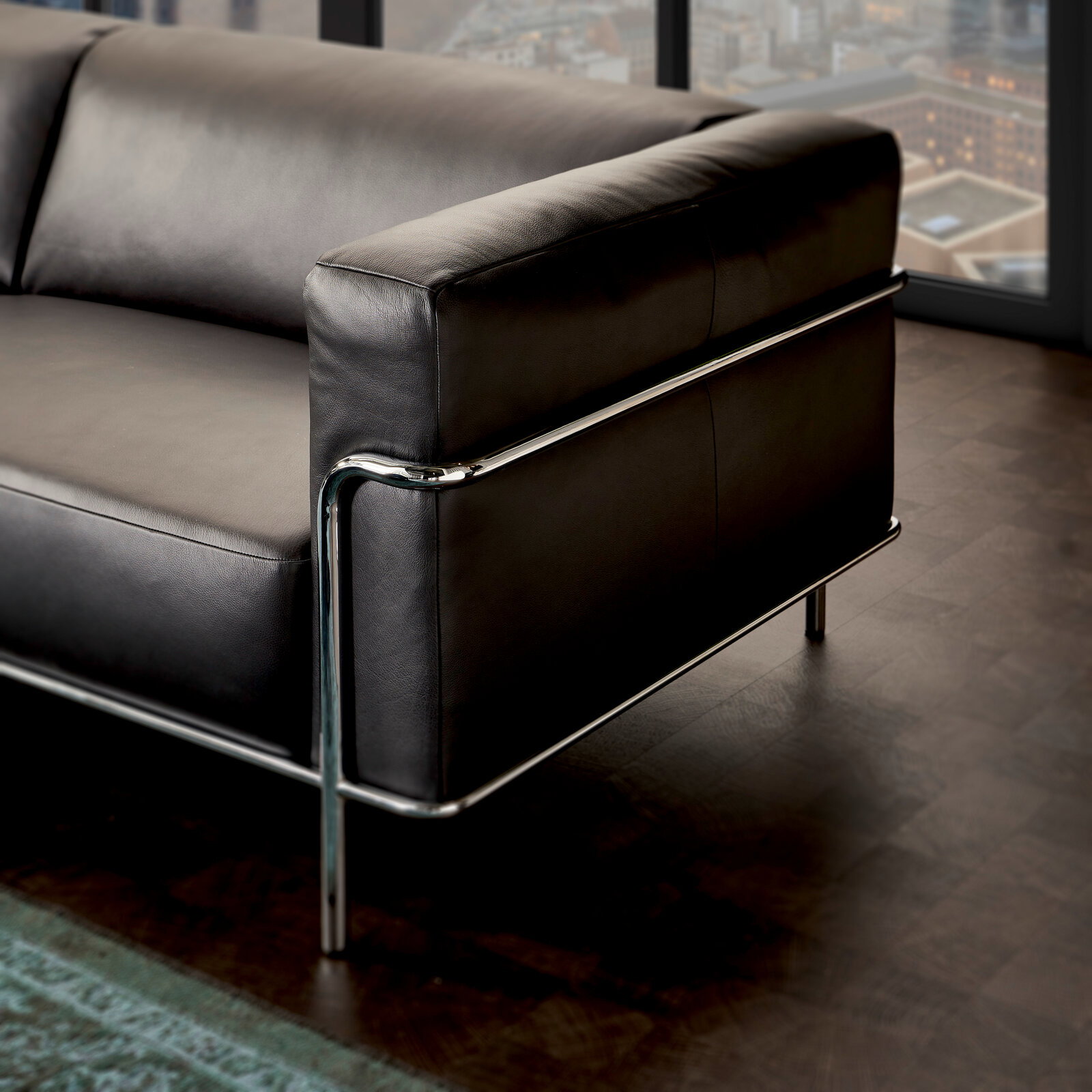 Modernes 3er-Sofa mit schwarzem Lederbezug und verchromtem Metallrahmen, seitliche Perspektive.