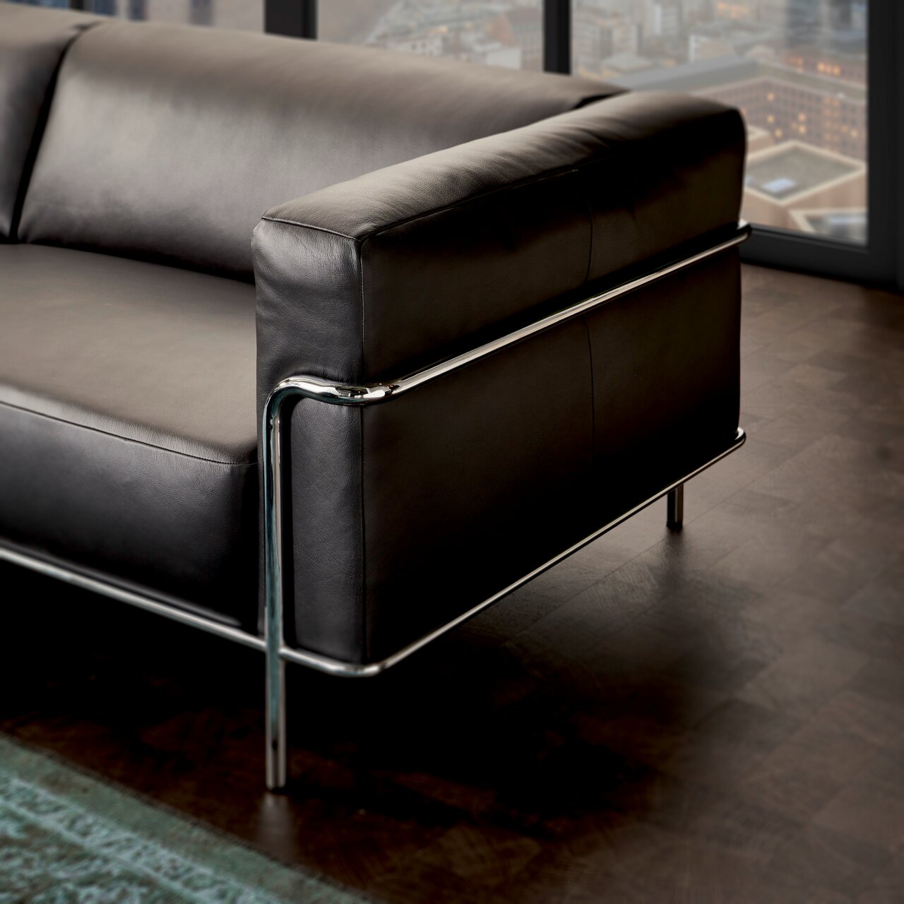 Moderne driezitsbank met zwarte lederen bekleding en verchroomd metalen frame, gezien vanaf de zijkant.