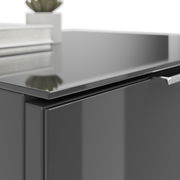 Nahaufnahme einer modernen, glänzenden Nachtkommode in dunkler Farbe mit einem Buch und einer Pflanze darauf.