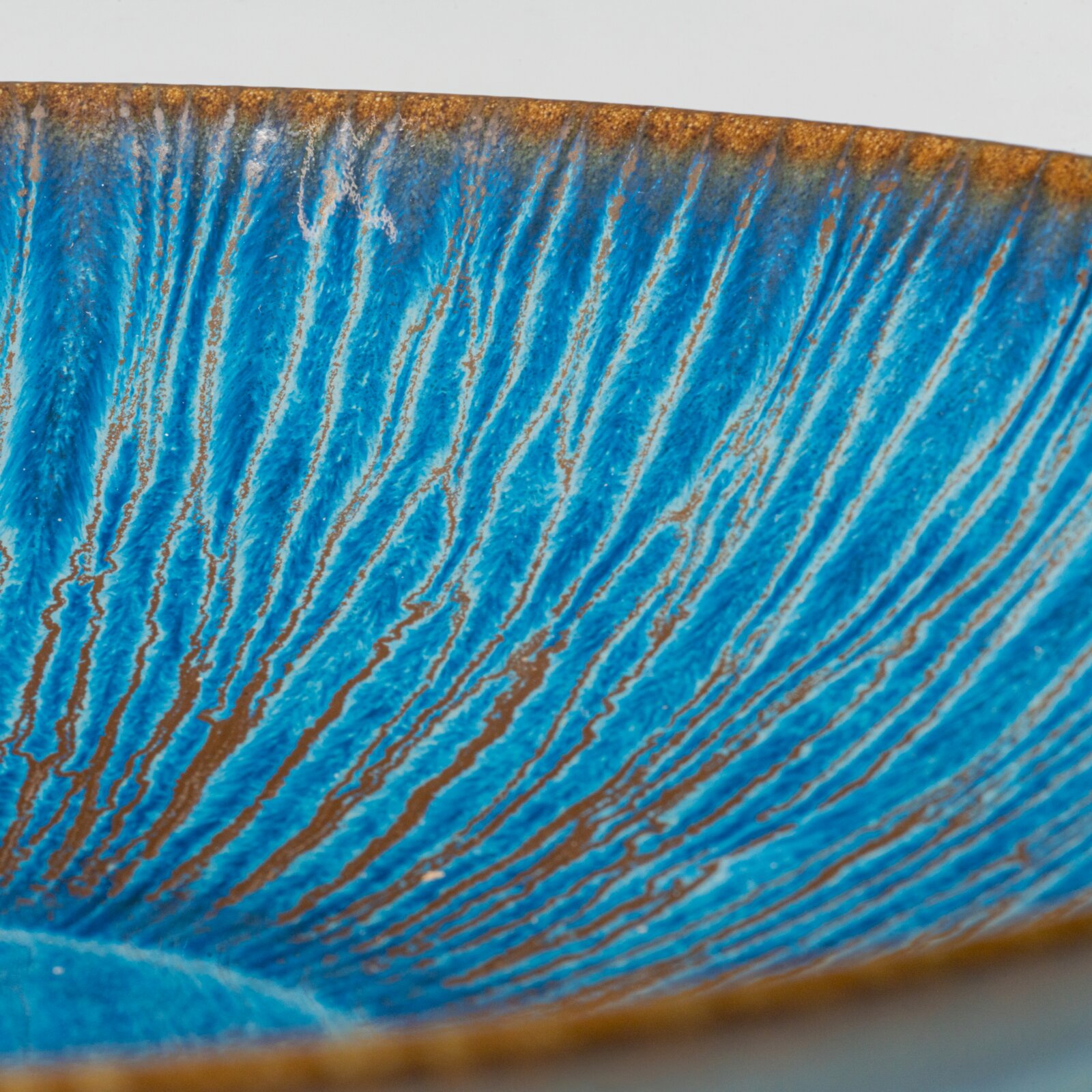 Detailaufnahme aus schräger Seitenperspektive einer glasierten Keramikschale mit blau-türkiser, streifiger Glasur und braunem Rand