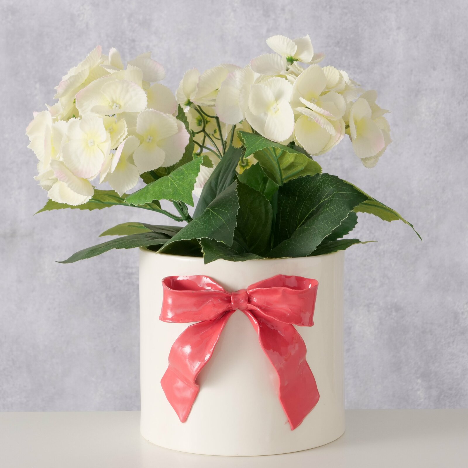 Porzellan-Übertopf mit roter Schleife und weißen Blumen, Frontalansicht