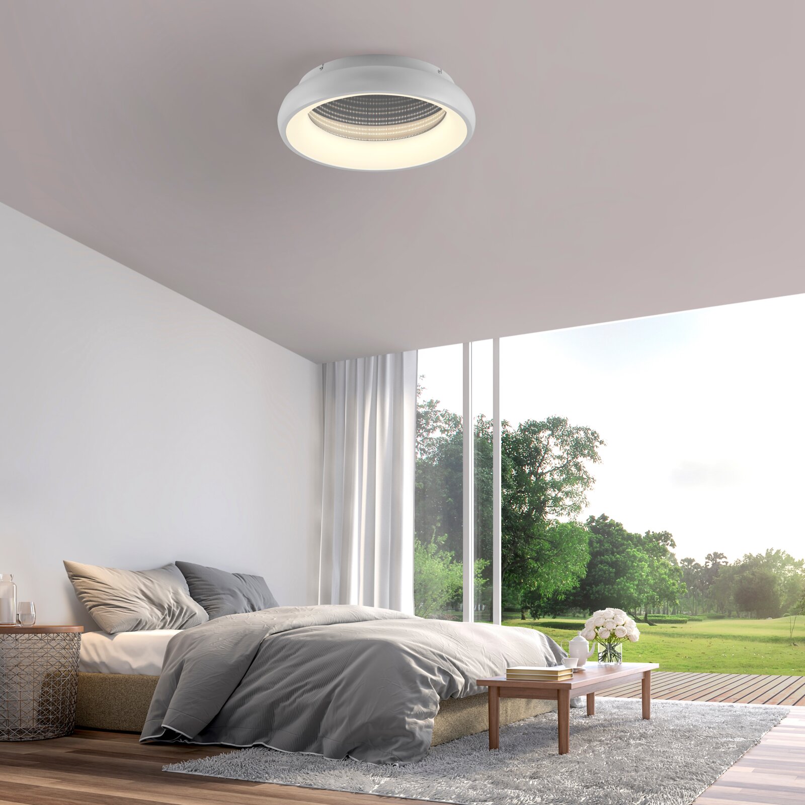 Moderne runde LED-Deckenleuchte in Weiß mit warmem Licht, an der Zimmerdecke montiert, Ansicht von unten in einem hellen Schlafzimmer mit großem Fenster und Blick ins Grüne