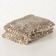 Leopardengemusterte Decke Leony aus weichem Material, gefaltet auf einem Tisch vor einer weißen Ziegelwand, seitliche Perspektive.