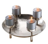 Dekorativer Kranz mit vier brennenden Kerzen auf einem silbernen, gehämmerten Teller, seitliche Perspektive.