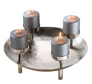 Dekorativer Kranz mit vier brennenden Kerzen auf einem silbernen, gehämmerten Teller, seitliche Perspektive.