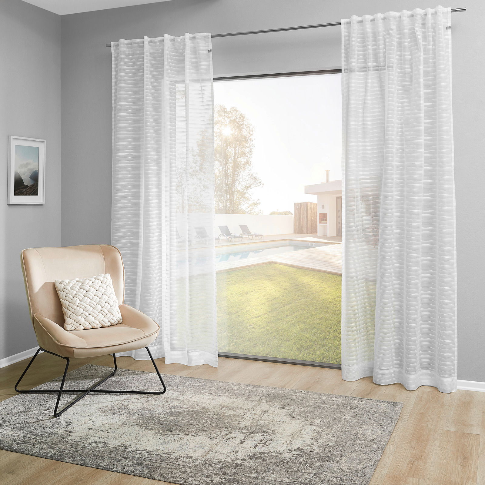 Weißer Dekoschal vor einem großen Fenster mit Blick auf einen Garten und Pool, seitliche Perspektive