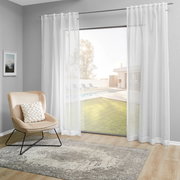 Weißer Dekoschal vor einem großen Fenster mit Blick auf einen Garten und Pool, seitliche Perspektive