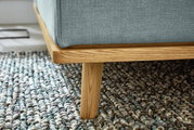 Close-up van een gestoffeerd bed met een lichtblauwe stoffen bekleding en een houten frame, gezien vanaf de zijkant.