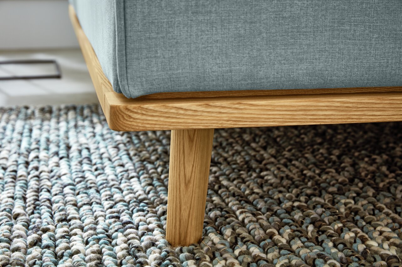 Close-up van een gestoffeerd bed met een lichtblauwe stoffen bekleding en een houten frame, gezien vanaf de zijkant.