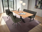 Moderner Esstisch aus Holz mit schwarzem Metallgestell, umgeben von gepolsterten Stühlen und einer Bank, in einem hellen Raum mit großen Fenstern, aus der Vogelperspektive betrachtet.