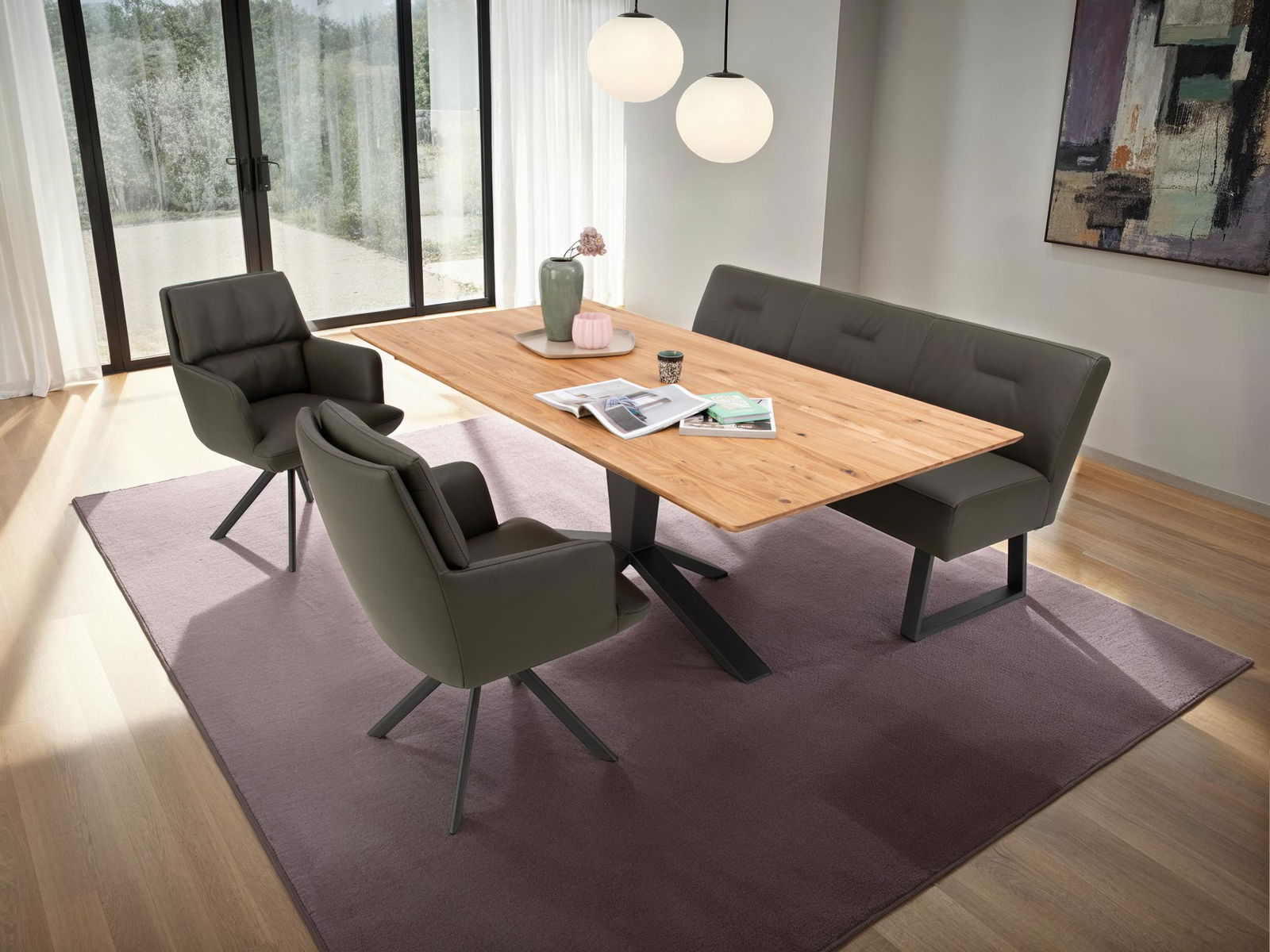 Moderner Esstisch aus Holz mit schwarzem Metallgestell, umgeben von gepolsterten Stühlen und einer Bank, in einem hellen Raum mit großen Fenstern, aus der Vogelperspektive betrachtet.