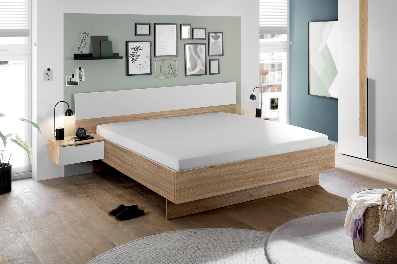 Modernes Schlafzimmer mit einem stilvollen Holzbett, flankiert von zwei Nachttischen mit Lampen. Die Wand ist mit Kunstwerken dekoriert. Perspektive: seitliche Ansicht des Bettes.