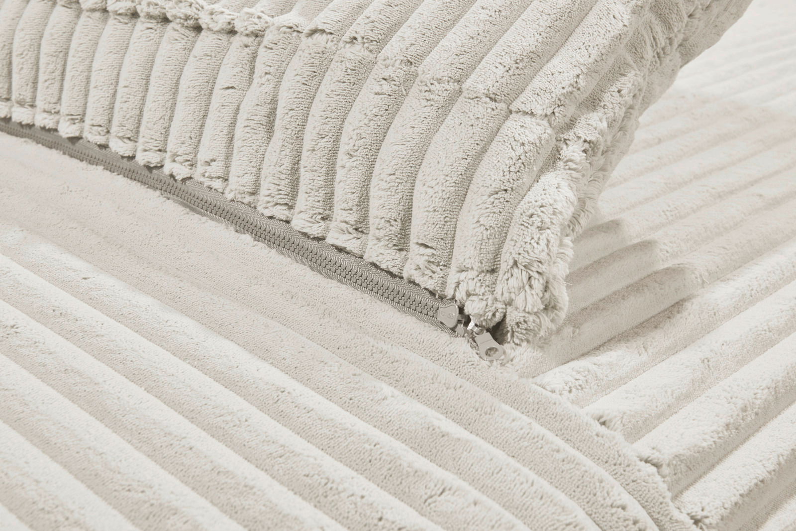 Nahaufnahme eines cremefarbenen Funktionssofas mit weichem, geripptem Stoff und sichtbarem Reißverschluss.