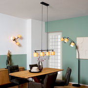 Moderne schwarze Pendelleuchte mit vier warm leuchtenden, zylindrischen Stoffschirmen über einem Holzesstisch im Esszimmer, Perspektive: frontale Raumansicht auf Augenhöhe.