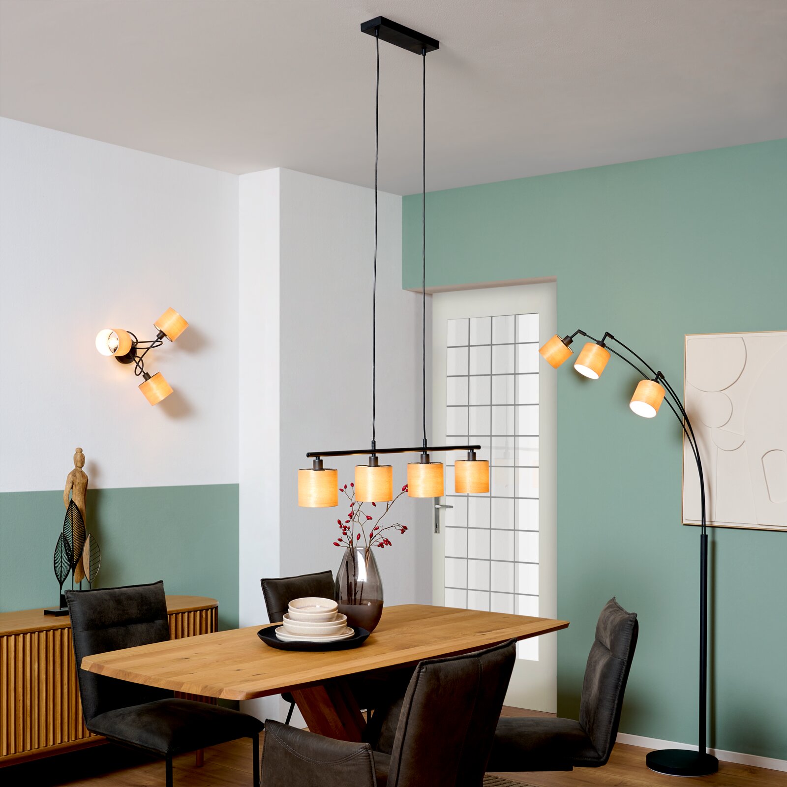 Moderne schwarze Pendelleuchte mit vier warm leuchtenden, zylindrischen Stoffschirmen über einem Holzesstisch im Esszimmer, Perspektive: frontale Raumansicht auf Augenhöhe.