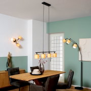 Moderne schwarze Pendelleuchte mit vier warm leuchtenden, zylindrischen Stoffschirmen über einem Holzesstisch im Esszimmer, Perspektive: frontale Raumansicht auf Augenhöhe.