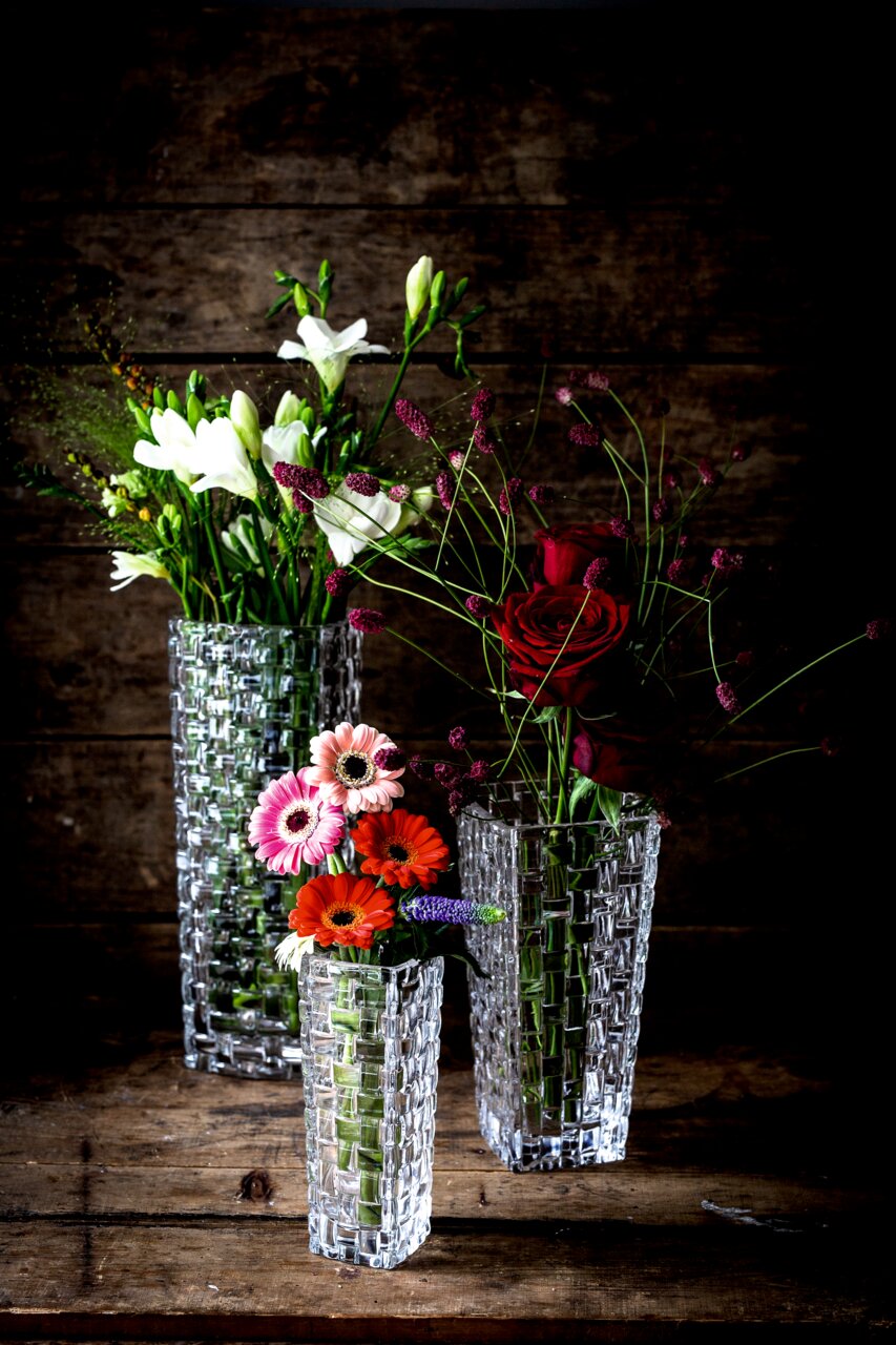 Nachtmann Vase 20cm BOSSA NOVA Drei elegante, klare Glasvasen mit Blumenarrangements, fotografiert aus einer leicht erhöhten Perspektive vor einem rustikalen Holzhintergrund.