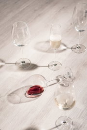 Vogelperspektive auf ein Set von Sektgläsern, eines gefüllt mit Sekt, auf einem hellen Holztisch.