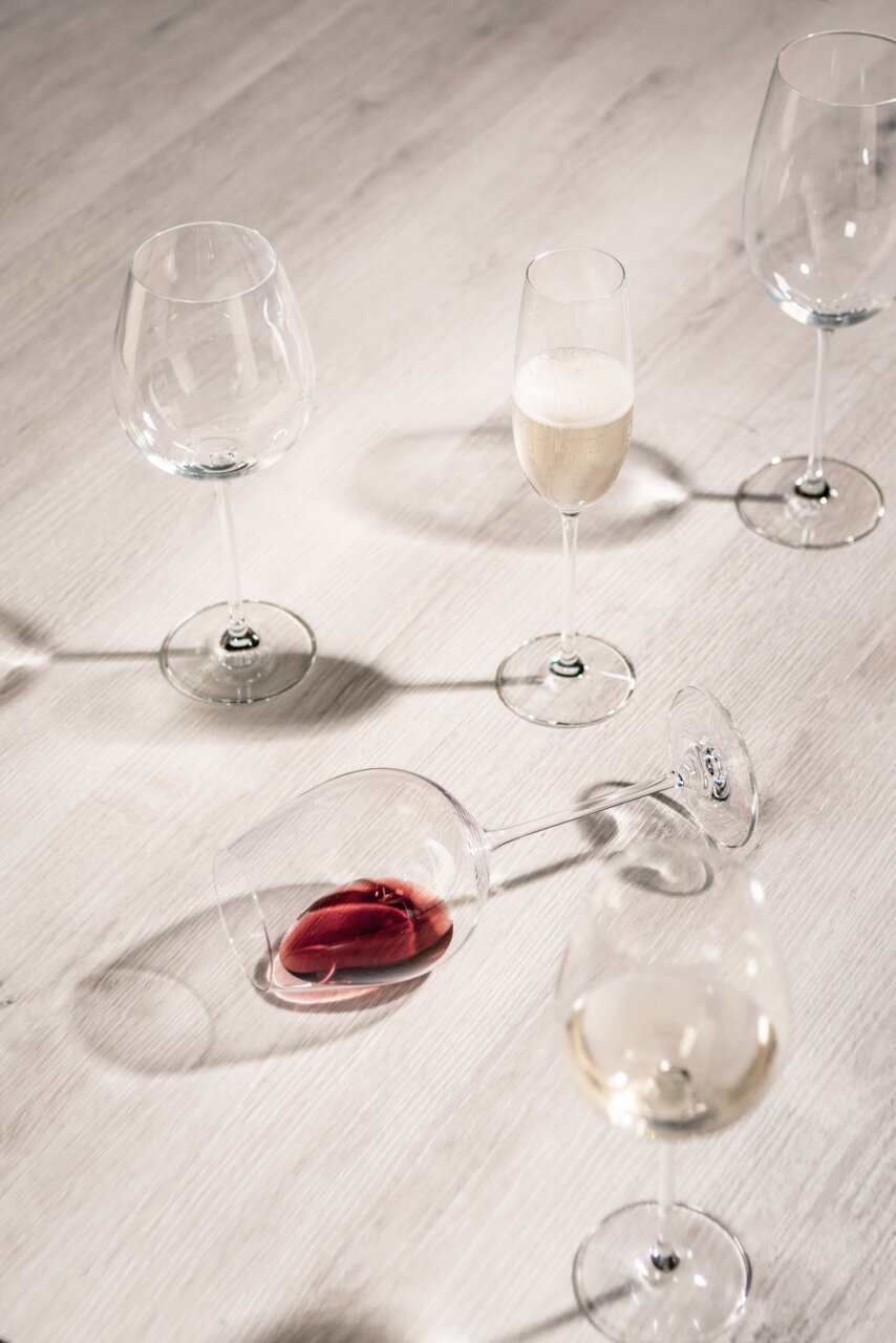 Vogelperspektive auf ein Set von Sektgläsern, eines gefüllt mit Sekt, auf einem hellen Holztisch.