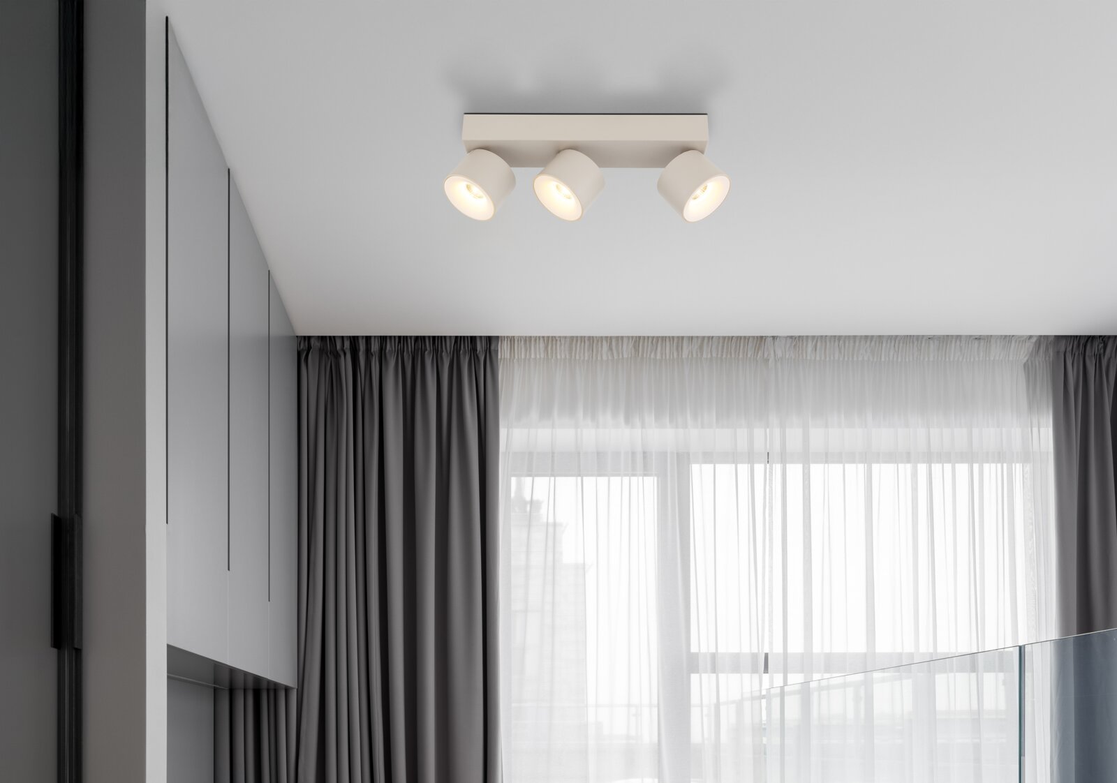 Moderne weiße Deckenleuchte mit drei verstellbaren Spotstrahlern auf rechteckiger Basis, warmes Licht, in minimalistischen Wohnraum – Ansicht von unten leicht seitlich