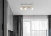 Moderne weiße Deckenleuchte mit drei verstellbaren Spotstrahlern auf rechteckiger Basis, warmes Licht, in minimalistischen Wohnraum – Ansicht von unten leicht seitlich