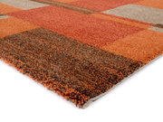 Nahaufnahme eines Frisé-Teppichs mit geometrischem Muster in warmen Orangetönen, aus seitlicher Perspektive fotografiert.
