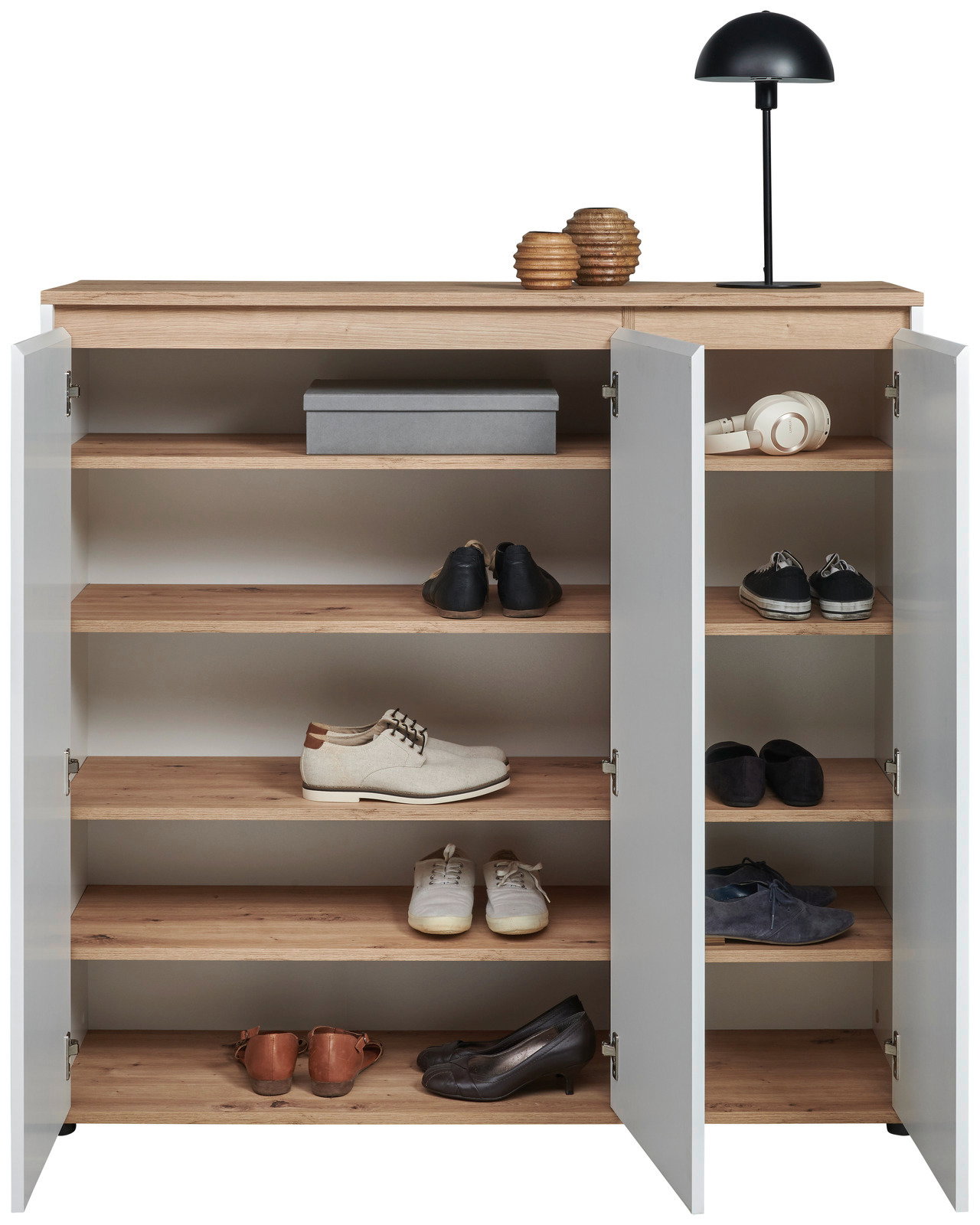 XL-Schuhschrank mit offenen Türen, gefüllt mit verschiedenen Schuhen, aus der Frontalperspektive fotografiert. Obenauf stehen eine Lampe und Dekorationsgegenstände.